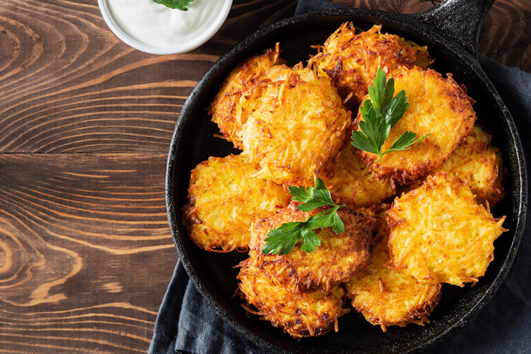 Potato latkes with garnish beside sour cream in an iron pan.