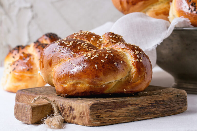 Challah bread on a wooden cutting board beside a bowl of bread