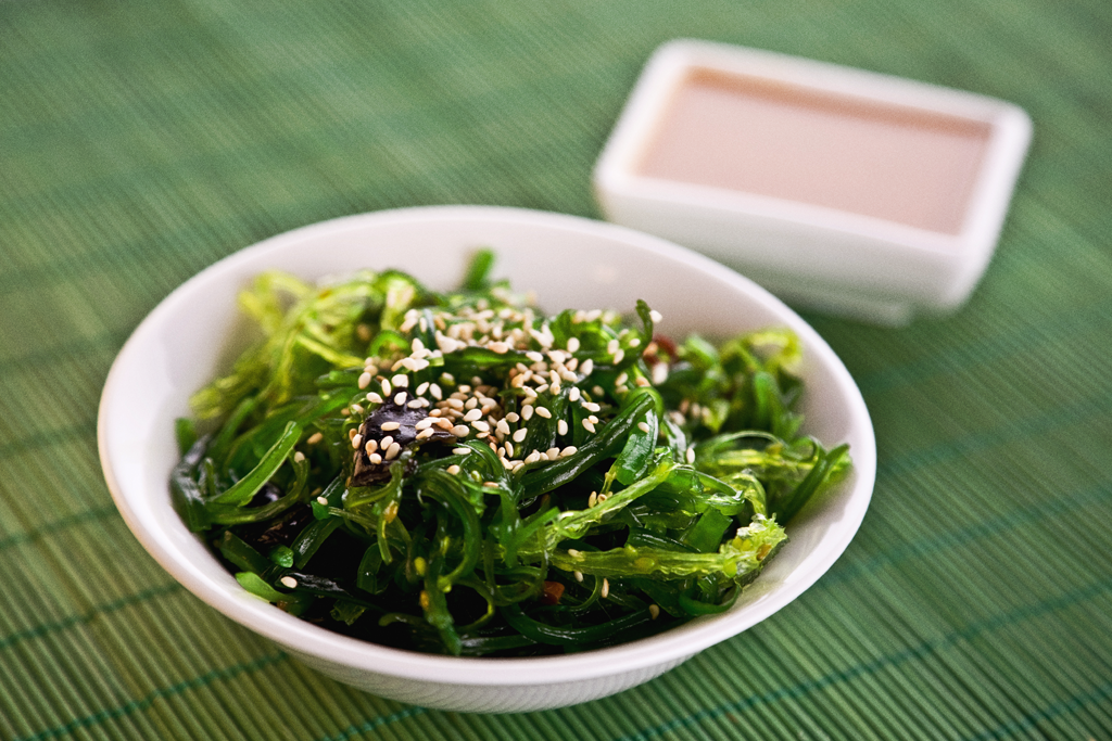 Seaweed salad in a white bowl on a placemat.