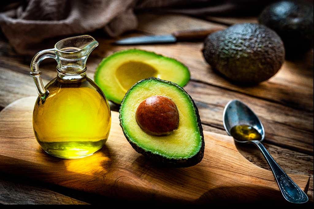 Halved avocado on a cutting board next to a jug of oil.