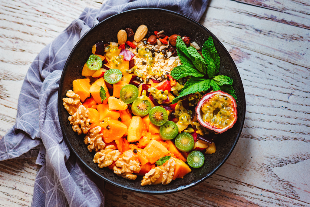 Smoothie bowl topped with fruit on a wooden table.