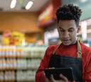 Convenience store owner using a tablet to create marketing ads for their business.