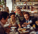 Restaurant employee dropping off an appetizer at a table of friends excited to take their first bite.