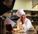 Chef in the back of kitchen on her laptop, working on her menu.
