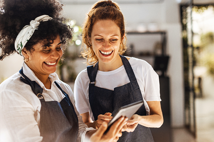wo happy women in aprons smiling at their tablet.