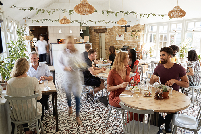  woman’s blurred figure serving customers at a busy boho styled restaurant.